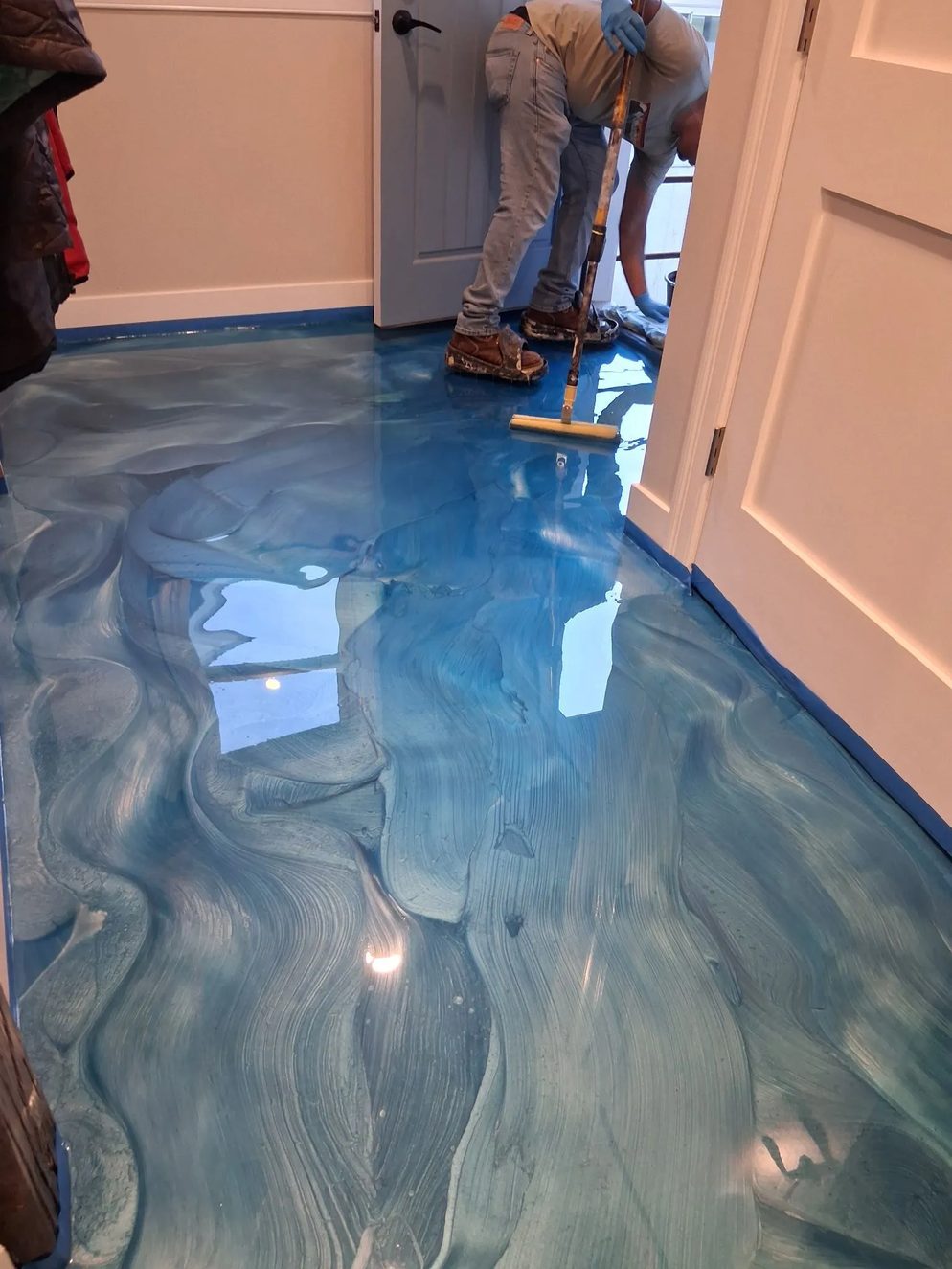 A blue metallic floor being spread with a squeegee while still wet